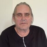 Rainer Mehlmann sitzt auf seinem Bett in seinem Zimmer im Pflegeheim. Er trägt eine Sauerstoffmaske und guckt in die Kamera.