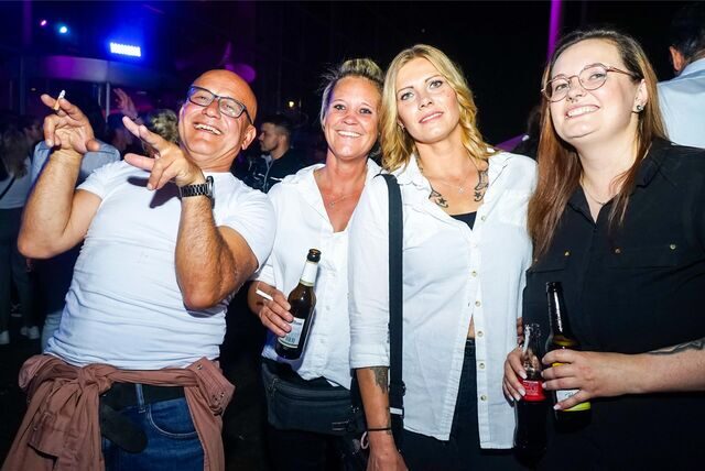 Ein Mann und drei Frauen stehen feixend beieinander, halten Zigaretten und Getränke in den Händen.