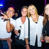 Ein Mann und drei Frauen stehen feixend beieinander, halten Zigaretten und Getränke in den Händen.