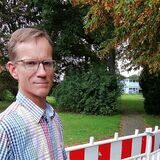 Schulleiter Ulrich Gerdesmeyer auf dem abseits gelegenen Teil des Schulareals mit dem abgebrannten Pavillon im Hintergrund.