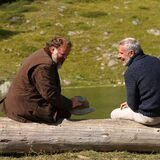Pierre (Grégory Gadebois, l.) und Vincent (Lambert Wilson) sitzen auf einem Baumstamm in der Natur und freunden sich an.