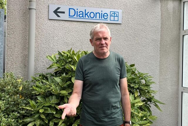 Mann steht vor dem Schild der Diakonie. Er schaut verärgert.