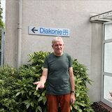 Mann steht vor dem Schild der Diakonie. Er schaut verärgert.