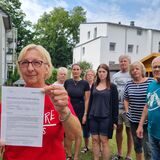 Eine Frau zeigt vor einer Gruppe Menschen ein Schriftstück