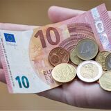 10€-Schein und einige Euro-Münzen in einer Hand