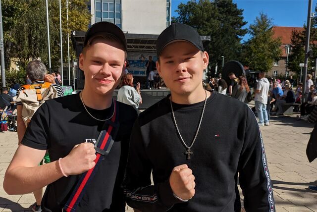 Zwei Jungen in Schwarz stehen vor einer Bühne.