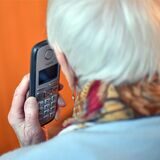 Eine Seniorin hält einen Telefonhörer an ihr Ohr (gestellte Szene).