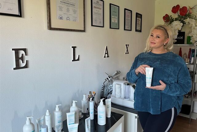 Olga Schäfer steht in ihrem Kosmetikstudio. Sie hält eine Tube Creme in der Hand. An der Wand hängen ihre Zertifikate, die sie als Kosmetikerin auszeichnen.