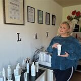 Olga Schäfer steht in ihrem Kosmetikstudio. Sie hält eine Tube Creme in der Hand. An der Wand hängen ihre Zertifikate, die sie als Kosmetikerin auszeichnen.