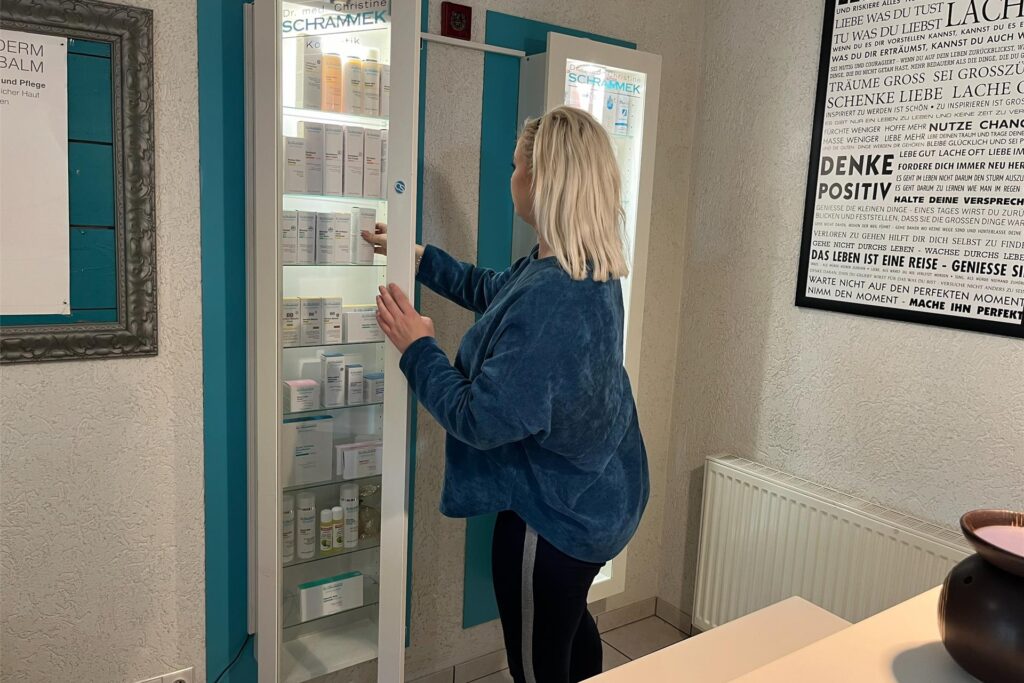 Olga Schäfer steht vor einer Vitrine und greift hinein. Sie steht hinter dem Empfang in ihren Kosmetikstudio. 