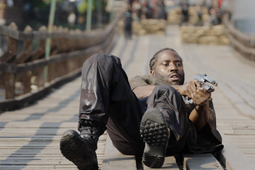 John David Washington spielt Josiah und liegt auf dem Boden mit einer Waffe in der Hand. John David Washington spielt Josiah und liegt auf dem Boden mit einer Waffe in der Hand.