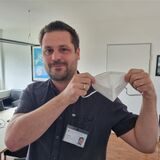 Ein Mann hält eine Schutzmaske hoch.