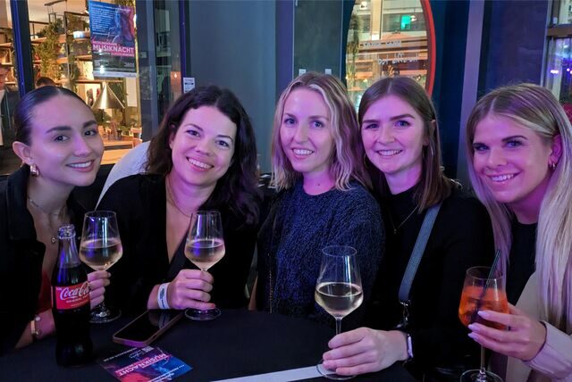 Fünf Frauen halten ein Getränk in der Hand und lächeln in die Kamera.