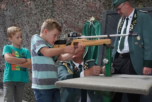 Ein Junge steht an einem Gewehr und zielt, dahinter ein Schütze in Uniform.