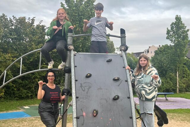 Drei Kinder und die Leiterin des Kinder- und Jugendparlaments stehen auf einem Klettergerüst. Mit ihren Daumen zeigen sie zur Seite. Damit signalisieren sie, wie sie die Lage der Spielplätze in Oer-Erkenschwick einschätzen.