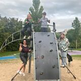 Drei Kinder und die Leiterin des Kinder- und Jugendparlaments stehen auf einem Klettergerüst. Mit ihren Daumen zeigen sie zur Seite. Damit signalisieren sie, wie sie die Lage der Spielplätze in Oer-Erkenschwick einschätzen.
