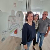 Zwei Frauen und ein Mann stehen vor einer Eingangstür