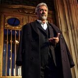 Mel Gibson in der Rolle des Hotel-Chefs Cornac O’Connor steht vor dem Eingang und blickt auf seine Taschenuhr.