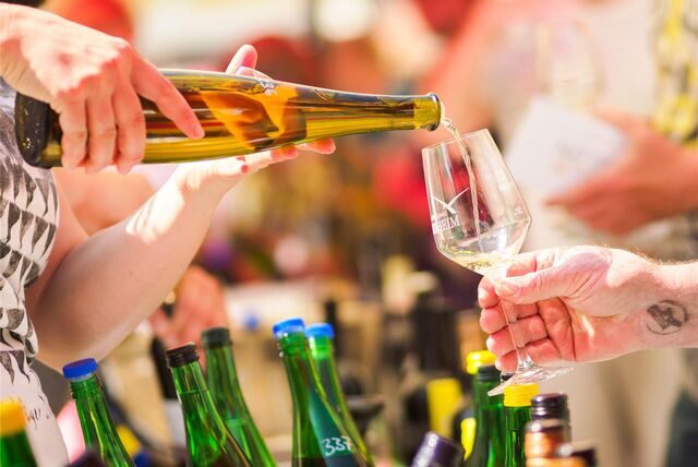 Eine Person schüttet einer anderen Person ein Glas Wein ein.