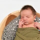 Ein Baby liegt im CKU Unna eingewickelt in eine grüne Decke auf einem Fell.