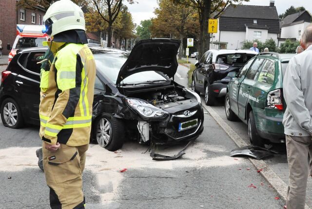 Die Kühlerhaube eines verunfallten Fahrzeugs ist geöffnet. Ein Feuerwehrmann steht davor.