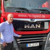 Spediteur Norbert Redemann steht in Recklinghausen vor einem roten Lkw, eine Hand liegt auf dem Kühlergrill.
