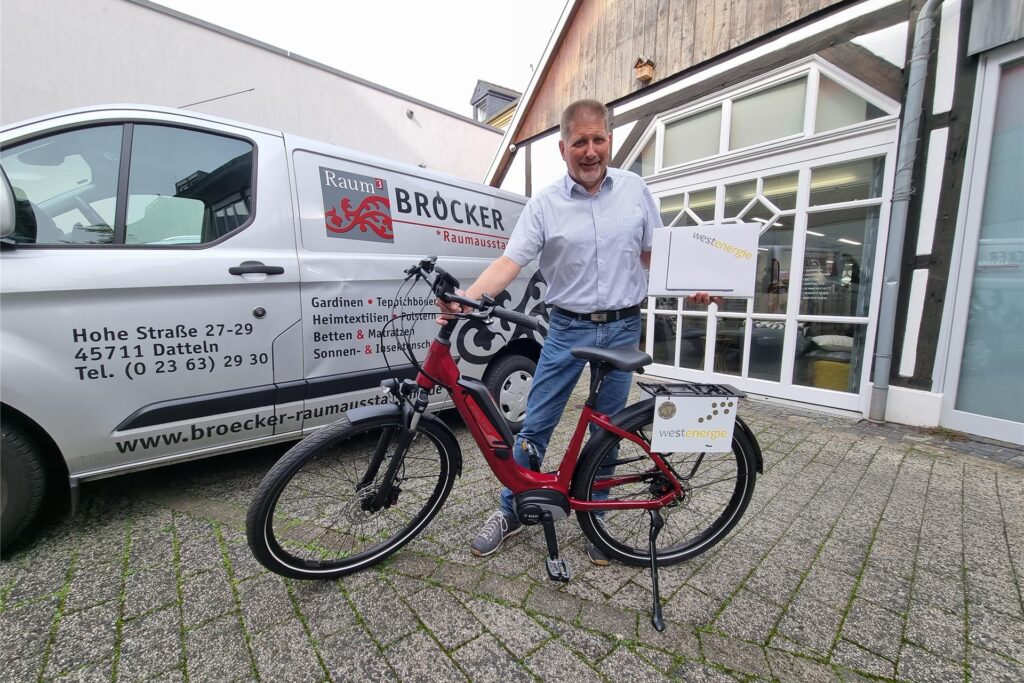 Ein Mann steht an einem E-Bike und hält ein MacBook Ein Mann steht an einem E-Bike und hält ein MacBook