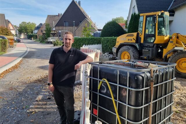 Ein Mann lehnt an einer Baustelle ab einer Absperrbake, im Hintergrund ein Bagger.