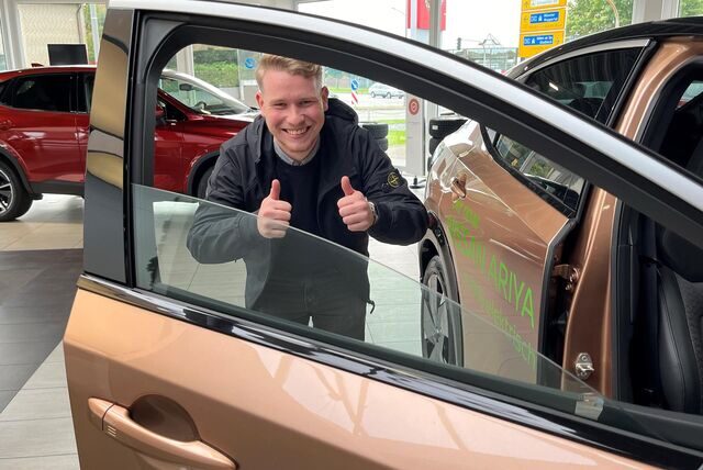 Ein junger Mann steht hinter dem Fensterrahmen eines Autos. Das Bild wurde in einem Autohaus aufgenommen.
