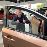 Ein junger Mann steht hinter dem Fensterrahmen eines Autos. Das Bild wurde in einem Autohaus aufgenommen.