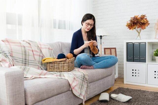 frau sitzt mit wolle und stricknadel auf der couch