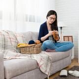 frau sitzt mit wolle und stricknadel auf der couch