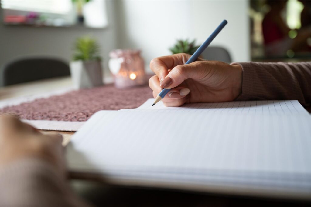 eine hand mit bleistift schreibt in ein heft