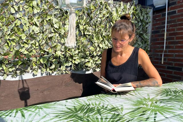 Eine Frau sitzt draußen auf einer Bank und liest ein Buch.