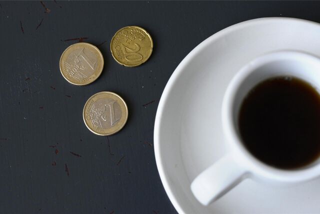 Münzen liegen neben einer Kaffeetasse auf einem Tisch