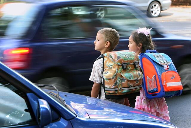 Kinder wollen eine Straße überqueren, Autos rasen vorbei.