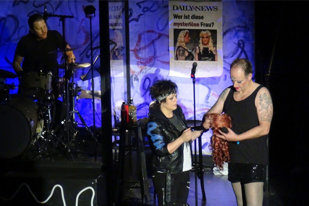 Hedwig geht also in die USA. Sie tourt als Rocksängerin mit ihrer Band „The Angry Inch“ durch die ganze Welt. Hedwig geht also in die USA. Sie tourt als Rocksängerin mit ihrer Band „The Angry Inch“ durch die ganze Welt.
