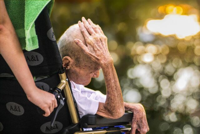 Ein alter Mann, der in einem Hospiz betreut wird, wird im Rollstuhl an die frische Luft gefahren.