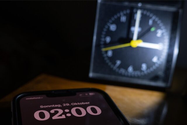 Ein Mann sitzt auf einem Bett und schaut genervt auf den Wecker