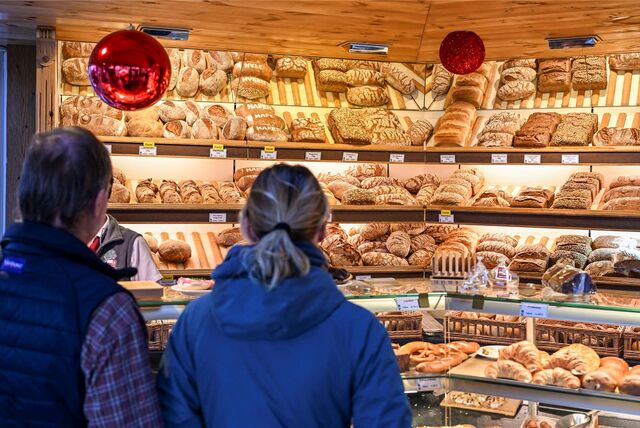 Zwei Kunden stehen in einer Bäckerei. Die Auslagen sind gut gefüllt.