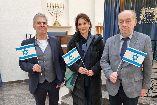 Isaac Tourgman, Bettina Kollecker und Dr. Mark Gutkin halten kleine Israel-Flaggen in der Synagoge in Recklinghausen in der Hand.