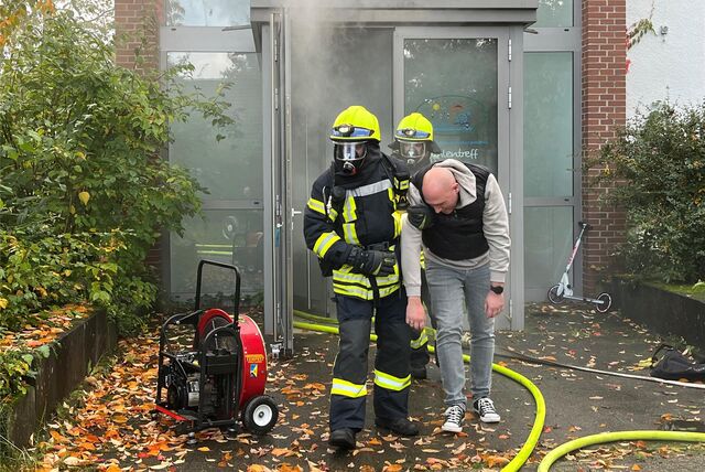 Zwei Feuerwehrleute führen eine Person aus dem verrauchten Mühlentreff.