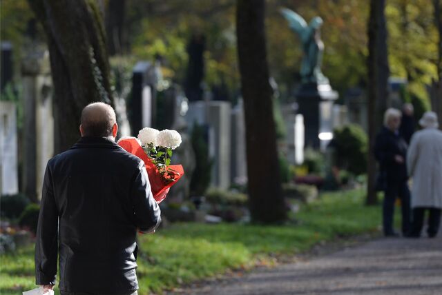 Ein Mann geht an Allerheiligen mit Blumen über den Friedhof. Am 01.11. ist Allerheiligen, ein christlicher Feiertag, an dem aller Heiligen und Toten gedacht wird.