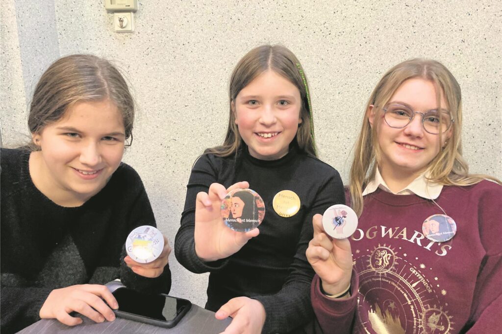 Drei Schülerinnen zeigen selbstgebastelte Buttons. Drei Schülerinnen zeigen selbstgebastelte Buttons.