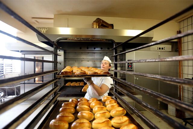 Eine Bäckerei-Fachverkäuferin holt frische Brötchen aus dem Ofen.