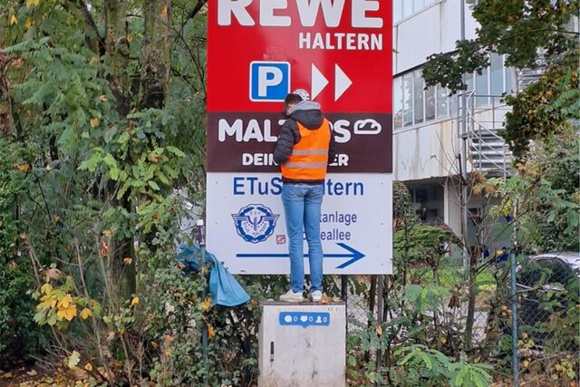 Junger Mann steht auf Stromkasten und reinigt Werbeschild.