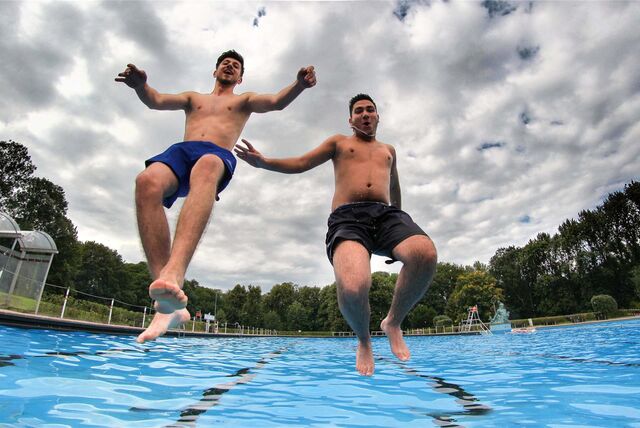 Zwei Männer springen in ein Freibad-Schwimmbecken