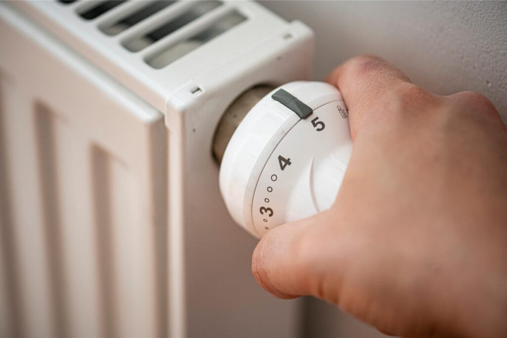 Eine Person dreht am Heizkörperthermostat 