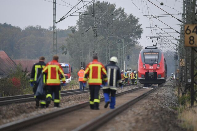 Rettungskräfte und ein Feuerwehrauto neben Bahngleisen mit Zug (Symbolbild).
