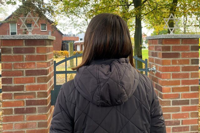 Eine Frau steht vor dem Eingangstor des jüdischen Friedhofs in Waltrop. Rechts und links ist jeweils ein Davidstern angebracht.